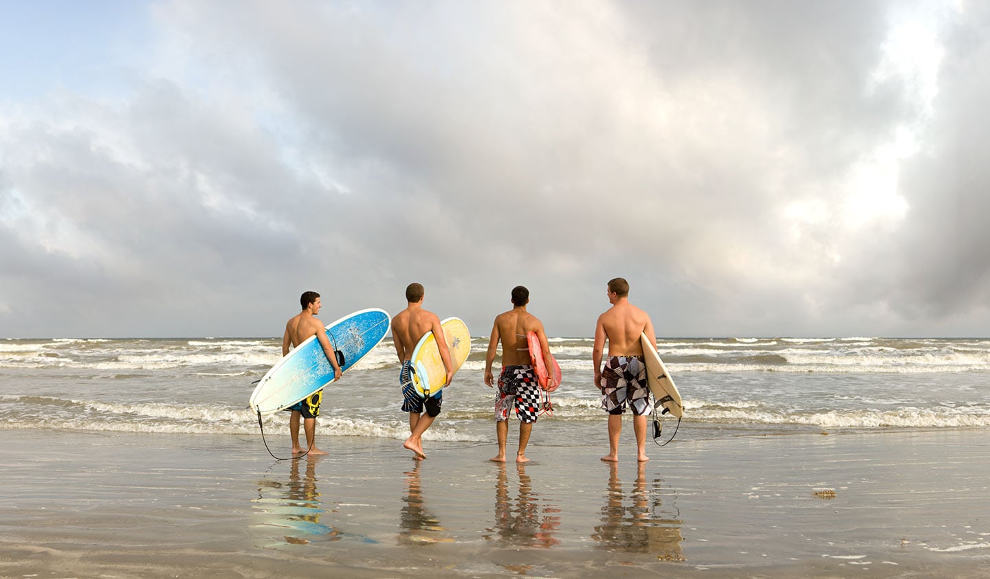 Back Image Four Men Entering Water With Surfboards Cloudy Beach