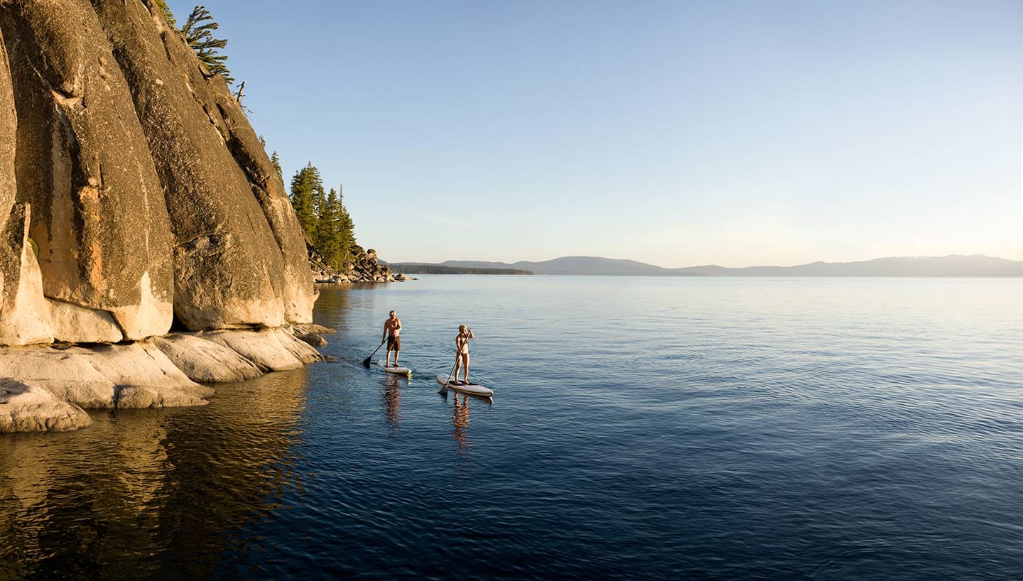 Man And Woman Standing on Surf Kayaks Paddling on Blue Water with Background of Blue Skies Cliff