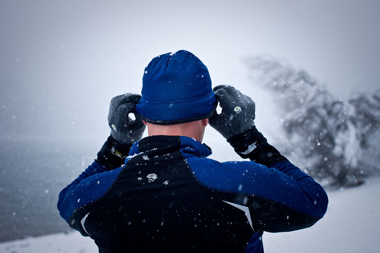 Man Wearing Blue Black Athletic Apparel Shot Behind Adjusting Hat Winter Snow