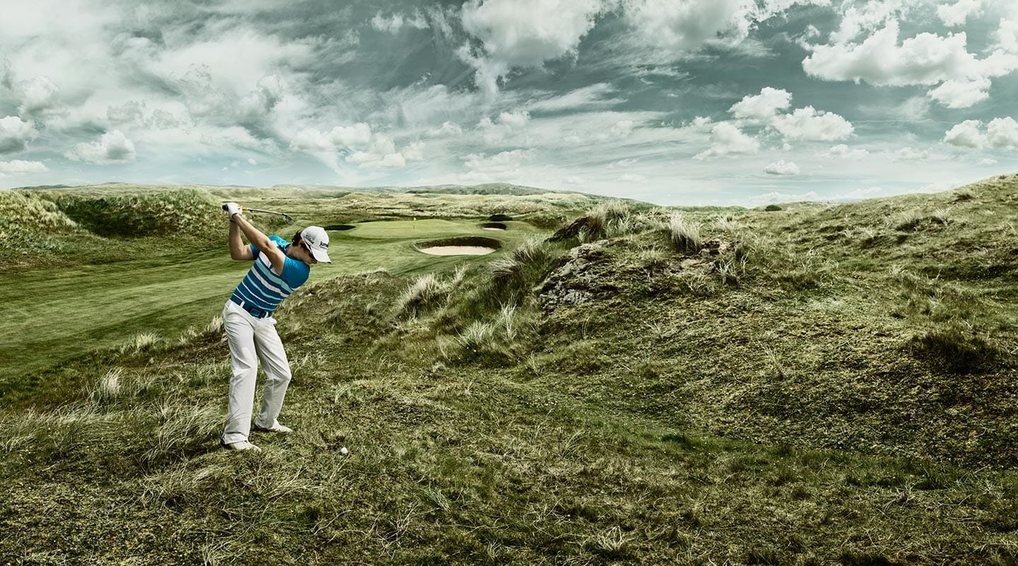 Man in Striped Shirt White Pants Mid Golf Swing Green Field Grey Skies Clouds