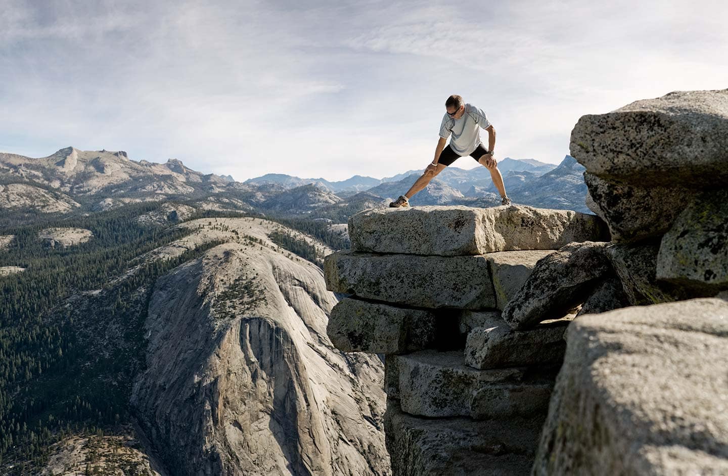 Runner in Black and White Athletic Apparel Stretching Over Rocks Against Background of Bright Skies