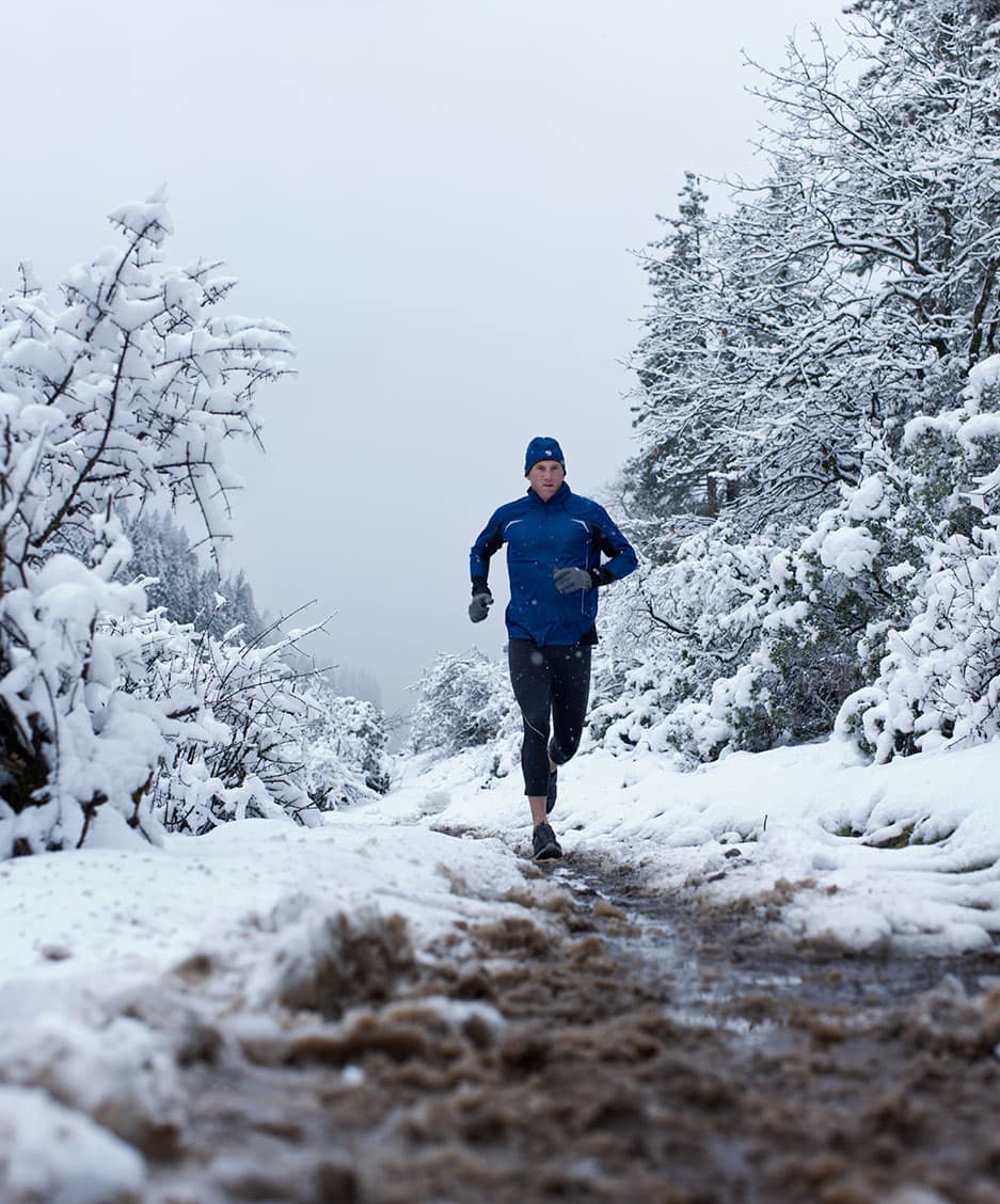 Runner in Blue Athletic Apparel Running in Cold Climate Against Snowy Background Front Perspective
