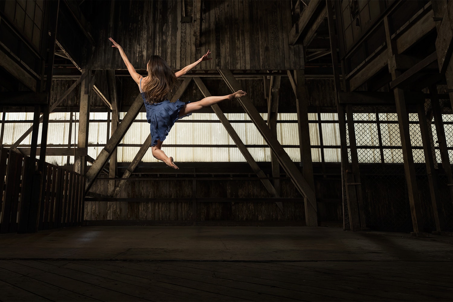 Female Ballerina Ballet jumping wearing a blue outfit dancing in a wood warehouse Photographer Rod McLean