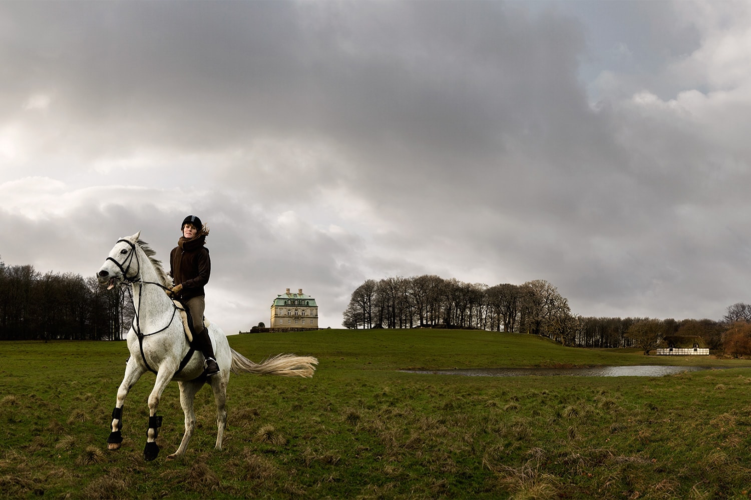 Female-riding-white-horse-in-a-field-in-front-of-castle-Rod-McLean