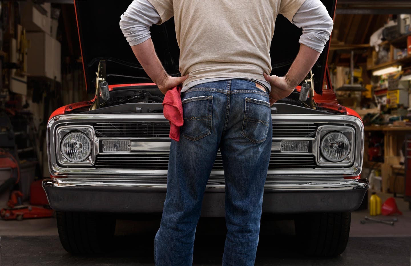 Image of Man from Behind in White Shirt and Blue Jeans with Red Hanky Standing Over Engine of Old Red Car